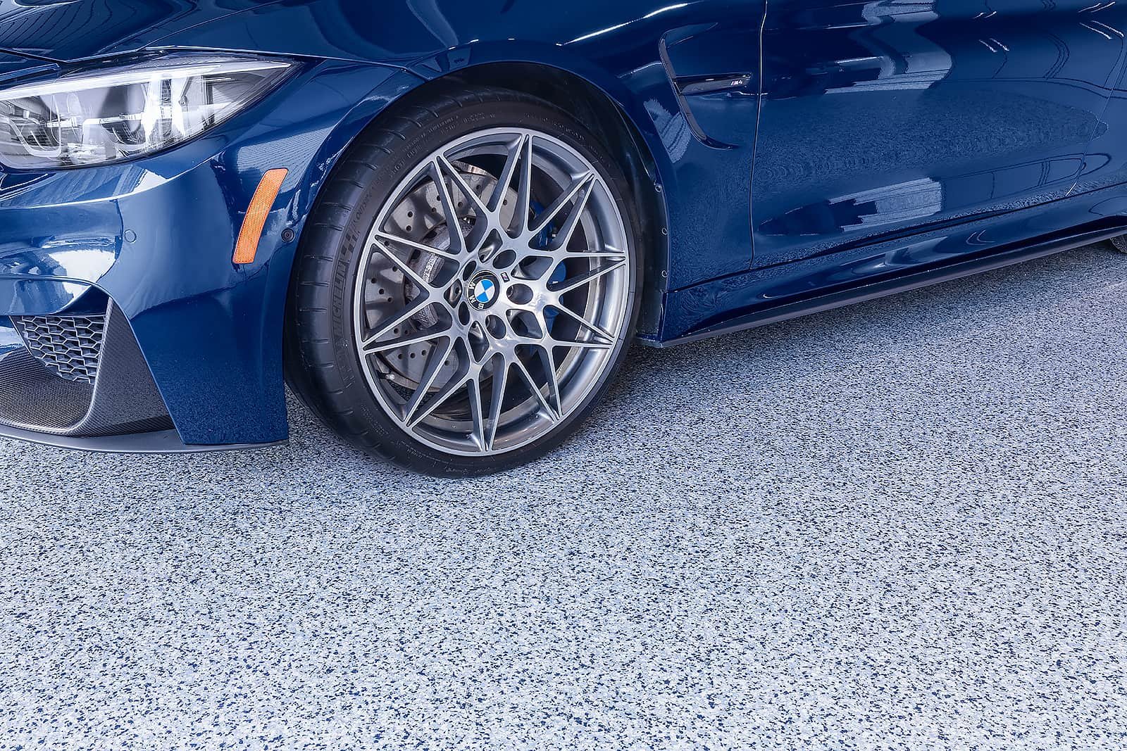 A BMW wheel is parked on a garage floor with a harbor blue coating, by Garage Living.