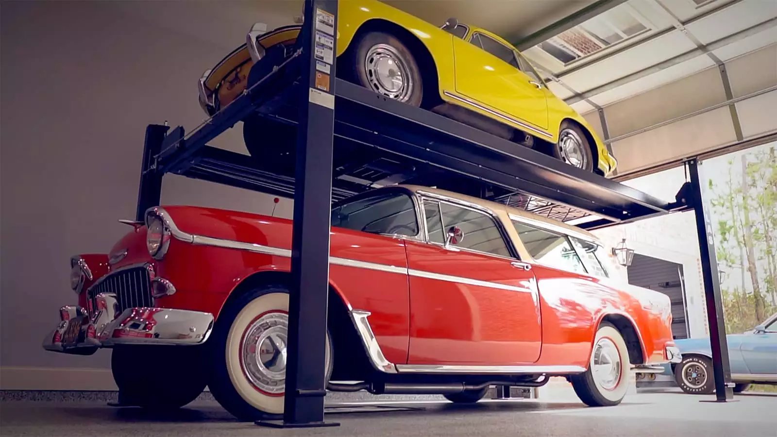 A car lift is raising two classic car by Garage Living